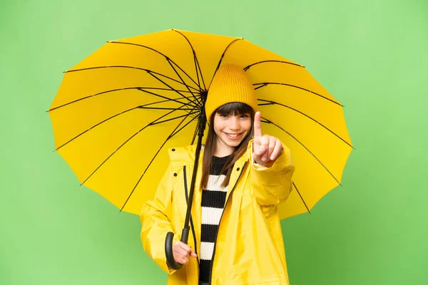 小さな女の子とともにレインプルーフコートと傘上の隔離されたクロマキー背景ショーと持ち上げ指 — ストック写真