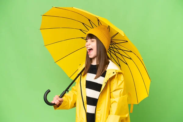 小さな女の子とともにレインプルーフコートと傘上の隔離されたクロマキー背景笑いますで横位置 — ストック写真