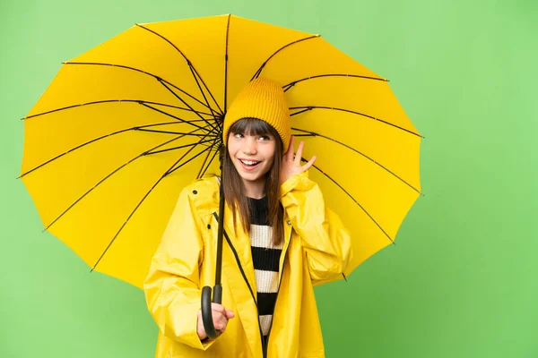 小さな女の子とともにレインプルーフコートと傘上の隔離されたクロマキー背景リスニング何かに手を置くことによって耳 — ストック写真