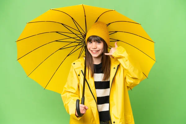 携帯電話のジェスチャーを作る隔離されたクロマキーの背景の上にレインプルーフコートと傘を持つ少女 サインを呼んでくれ — ストック写真