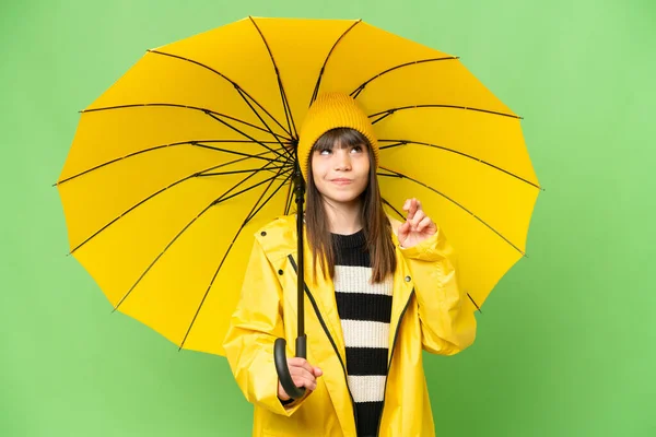 小さな女の子とともにレインプルーフコートと傘上の隔離されたクロマキー背景とともに指交差と願いますザベスト — ストック写真