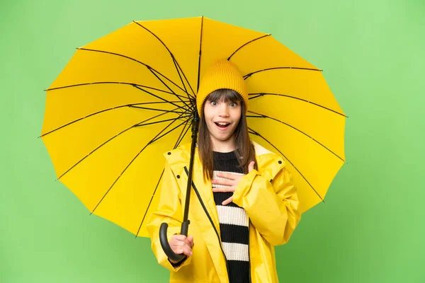 小さな女の子とともにレインプルーフコートと傘上の隔離されたクロマキー背景驚きとショックを受けながら右見て — ストック写真