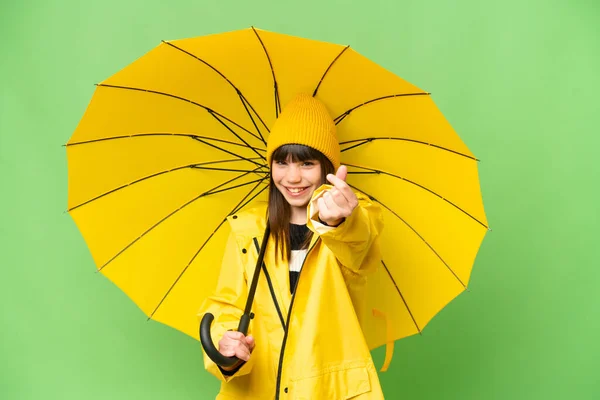 小さな女の子とともにレインプルーフコートと傘上の隔離されたクロマキー背景作りお金ジェスチャー — ストック写真