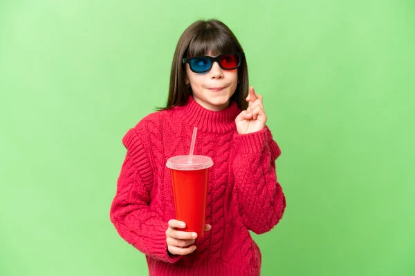 Little girl holding soda over isolated chroma key background with fingers crossing and wishing the best