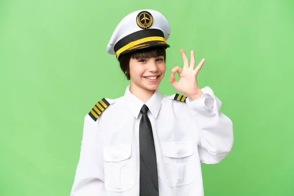 小女孩作为飞机驾驶员 在孤立的彩色背景下 用手指显示出确定的标志 — 图库照片