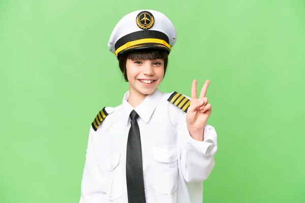 小女孩作为飞机驾驶员在孤立的彩色背景下微笑着并展示胜利的标志 — 图库照片