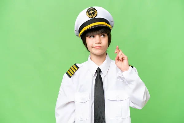 Little girl as a Airplane pilot over isolated chroma key background with fingers crossing and wishing the best