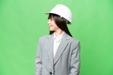 Küçük kız miğferiyle mimar olarak oynuyor ve arka planda izole edilmiş planlar tutuyor.