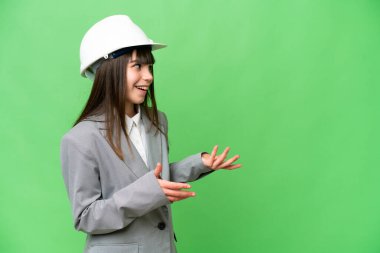 Miğferli bir mimar gibi davranan küçük bir kız, yalıtılmış bir arka plan üzerinde sürpriz bir ifadeyle planlar tutuyor.