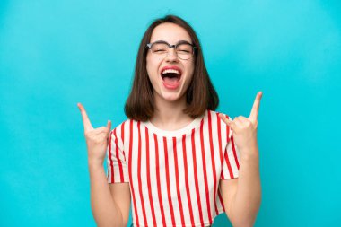 Mavi arka planda izole edilmiş genç Ukraynalı kadın boynuz hareketi yapıyor.