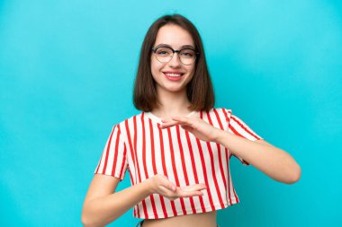 Mavi arka planda izole edilmiş genç Ukraynalı bir kadın bir ilan vermek için avucunun içinde hayali bir kopyalama alanı tutuyor.