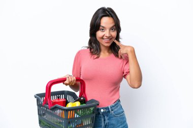 Elinde yiyecek dolu bir alışveriş sepetini tutan genç bir kadın baş parmak işareti yapıyor.