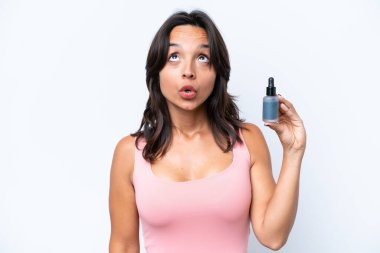 Beyaz arka planda serumu tutan genç İspanyol kadın şaşırmış bir ifadeyle yukarı bakıyor.