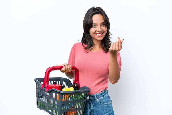 一个拿着装满食物的购物篮的年轻女人做着赚钱的姿势 — 图库照片