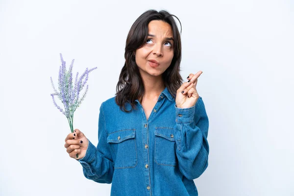 Young hispanic woman holding lavender isolated on white background with fingers crossing and wishing the best