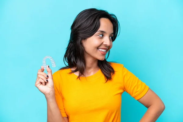 Young hispanic woman holding invisible braces isolated on blue background looking side