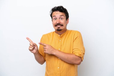 Bıyıklı genç adam beyaz arka planda izole edilmiş korkmuş ve kenarı işaret ediyor.