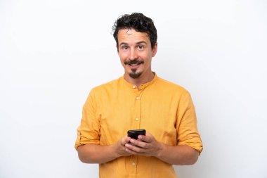 Bıyıklı genç adam beyaz arka planda izole edilmiş cep telefonuyla mesaj gönderiyor.