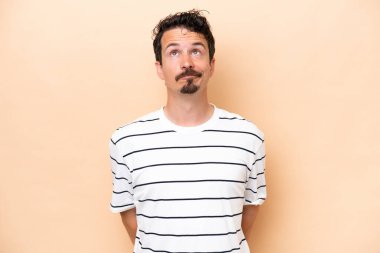 Beyazlı genç bir adam bej arka planda izole edilmiş ve araştırılıyor.