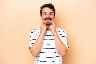 Beyaz tenli genç adam bej arka planda izole edilmiş mutlu ve hoş bir ifadeyle gülümsüyor.