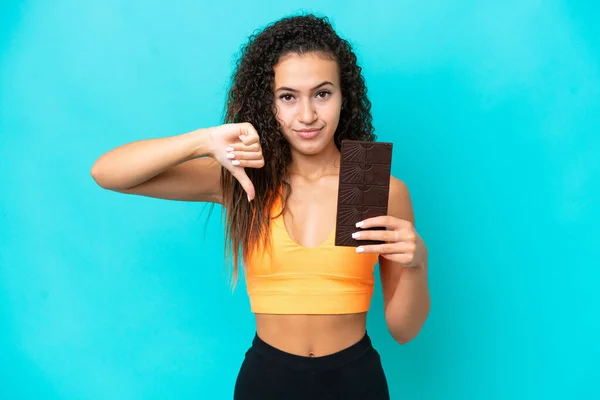 Young Arab woman isolated on blue background taking a chocolate tablet making bad signal