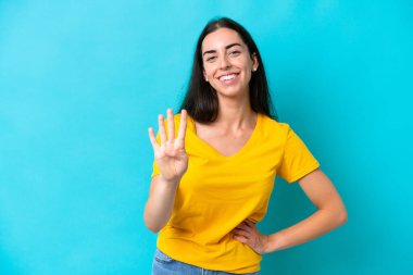 Mavi arka planda izole edilmiş genç beyaz kadın mutlu ve parmaklarıyla dörde kadar sayıyor.