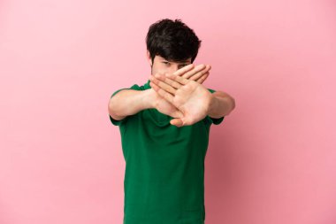 Pembe arka planda izole edilmiş genç bir Rus adam bir hareketi durdurmak için eliyle jest yapıyor.