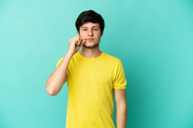 Mavi arka planda izole edilmiş genç bir Rus adam sessizlik işareti gösteriyor.