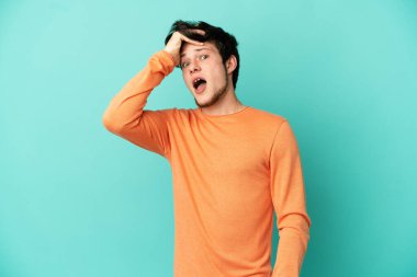 Mavi arka planda izole edilmiş genç bir Rus, yan tarafa bakarken sürpriz jest yapıyor.