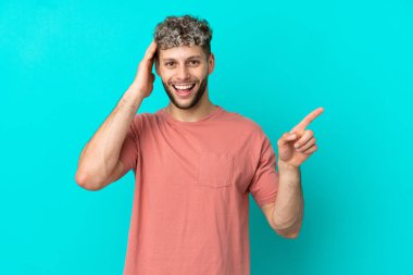 Mavi arka planda izole edilmiş yakışıklı beyaz adam şaşırdı ve parmağını yana çevirdi.