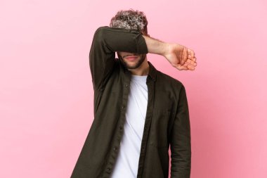 Pembe arka planda izole edilmiş yakışıklı beyaz adam gözleri elleriyle kapatıyor.