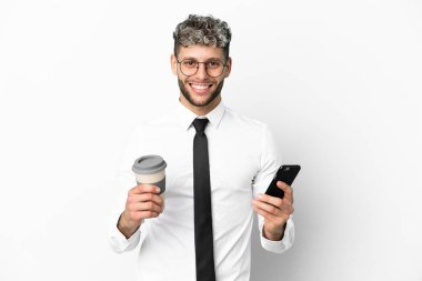 Beyaz arka planda izole edilmiş beyaz bir iş adamı elinde kahve ve bir cep telefonu tutuyor.