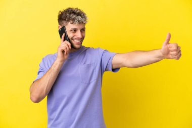 Sarı arka planda izole edilmiş cep telefonu kullanan beyaz bir adam işaret veriyor.