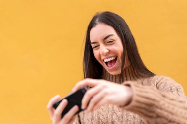 Genç esmer kadın dışarıda cep telefonuyla oynuyor.