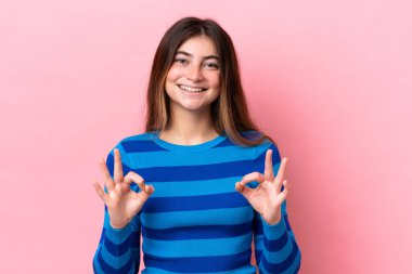 Pembe arka planda izole edilmiş beyaz bir kadın iki eliyle tamam işareti gösteriyor.