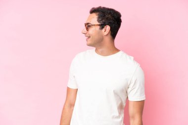 Pembe arka planda izole edilmiş genç beyaz adam yana bakıyor ve gülümsüyor.