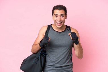 Spor çantalı beyaz bir genç, pembe arka planda izole edilmiş bir şekilde galibiyeti kutluyor.