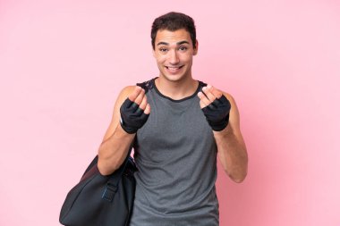 Spor çantalı genç beyaz adam pembe arka planda izole edilmiş para hareketi yapıyor.