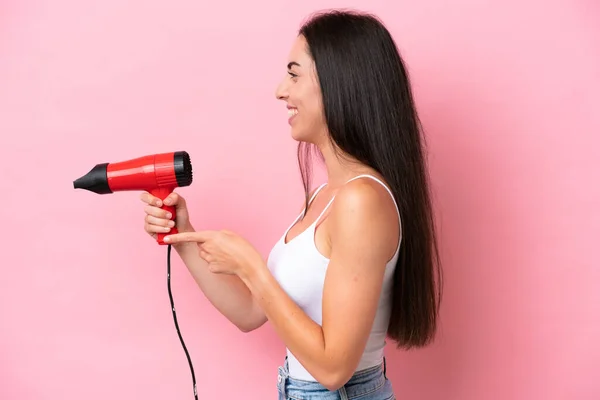 Jonge Blanke Vrouw Met Een Haardroger Geïsoleerd Roze Achtergrond Wijzend — Stockfoto