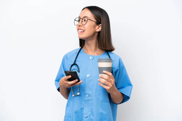 年轻的外科医生女医生被隔离在白色背景下 一边拿着咖啡一边想着什么 一边拿着手机走了 — 图库照片