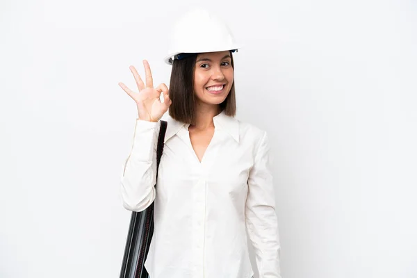 ヘルメットを持つ若い建築家の女性と指でOkサインを示す白い背景に隔離された設計図を保持 — ストック写真