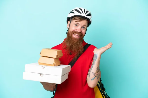 Delivery man holding pizzas and burgers isolated on blue background extending hands to the side for inviting to come