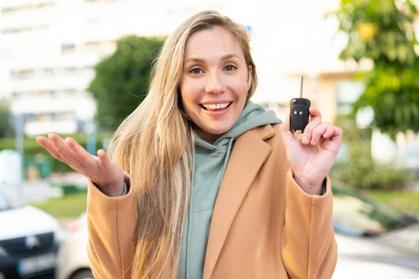 Ung Blond Kvinna Håller Bilnycklar Utomhus Med Chockad Ansiktsuttryck — Stockfoto