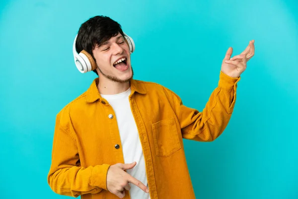 Joven Ruso Aislado Sobre Fondo Azul Escuchando Música Haciendo Gesto — Foto de Stock