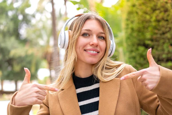 Νεαρή Όμορφη Ξανθιά Γυναίκα Ακούει Μουσική Ακουστικά Εξωτερικούς Χώρους Υπερήφανη — Φωτογραφία Αρχείου