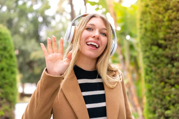 Молодая Красивая Блондинка Слушает Музыку Наушниках Открытом Воздухе Салютуя Рукой — стоковое фото