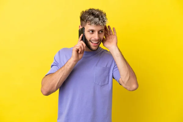Młody Biały Człowiek Pomocą Telefonu Komórkowego Odizolowany Żółtym Tle Słuchanie — Zdjęcie stockowe