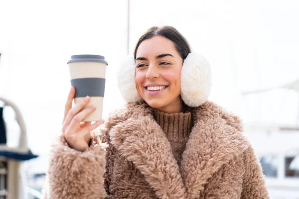 年轻女人穿着冬衣 拿着咖啡 满面春风地在户外喝咖啡 — 图库照片
