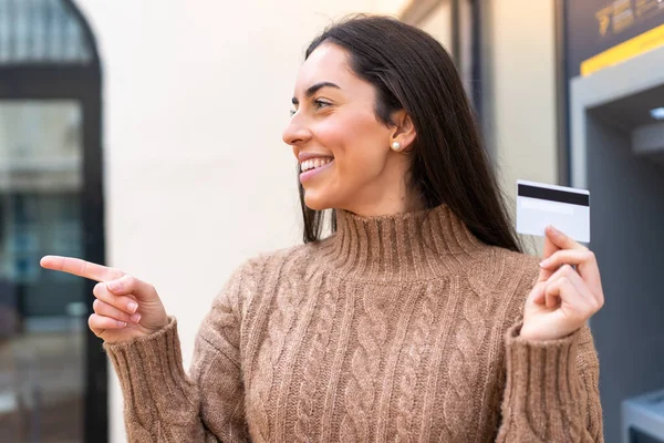 Młoda Kobieta Kartą Kredytową Zewnątrz Wskazując Bok Aby Przedstawić Produkt — Zdjęcie stockowe