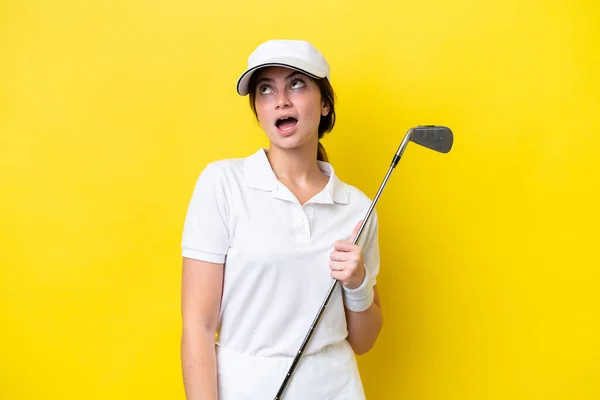 年轻的高加索女人打高尔夫球时 背景是黄的 抬头一看 满脸诧异 — 图库照片
